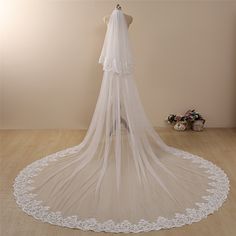 a white wedding veil on a mannequin in front of a wall with flowers