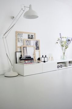 a white shelf with pictures and books on it next to a lamp, flowers and other items