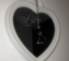 a heart shaped mirror with a spider web hanging from it's center, in front of a white wall