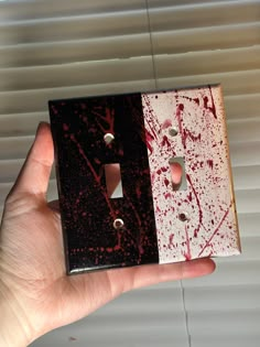 a hand holding a light switch cover with red paint on it