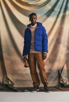 a man standing in front of a backdrop wearing a blue puffy jacket and tan pants