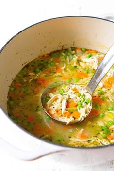 a ladle full of chicken noodle soup with peas and carrots