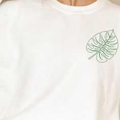 a close up of a person wearing a white shirt with a green leaf on it