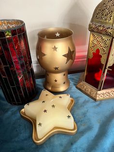 three decorative items on a blue table cloth next to a lit candle and lantern holder