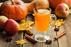 a glass mug filled with apple cider next to apples, cinnamons and pumpkins