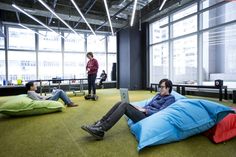 two people sitting on bean bag chairs in an office setting with one person using a laptop