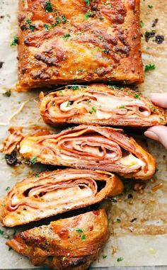 someone is holding up some bread with meat and cheese in it on a sheet of baking paper