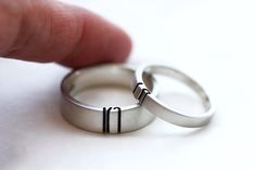 two silver wedding rings with black lines on the inside of them, being held by a finger