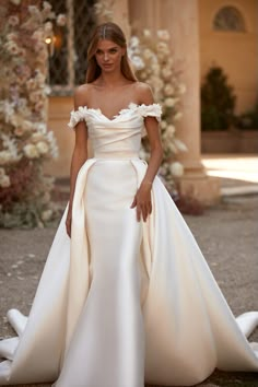 a woman in a white wedding dress standing on the ground with her hands behind her back