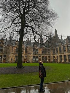 a man standing in front of a large building with a tree on the side of it