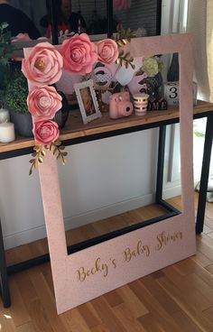 there is a pink baby shower sign on the shelf with flowers and pictures in it