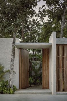 two wooden doors are open in front of a concrete structure with trees and bushes around it