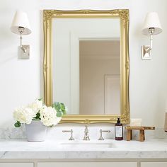 a bathroom vanity with a large mirror above it and flowers in a vase on the counter