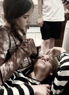 a woman is getting her hair combed by a man in striped shirt and black shorts