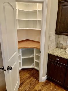 an empty pantry in the corner of a room with wooden floors and cabinets on either side