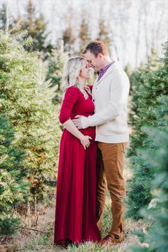 a pregnant couple standing next to each other in the middle of a christmas tree farm