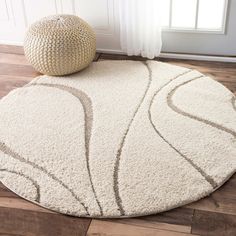 a white rug with an abstract design on the floor next to a round ottoman in front of a window