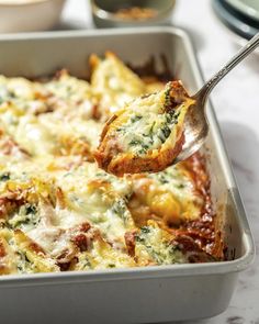 a casserole dish with spinach and cheese being scooped from it