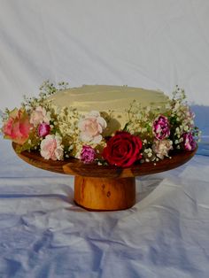 there is a cake with flowers on it sitting on a wooden platter, ready to be served