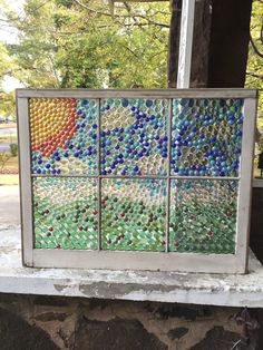 an old window has been decorated with colorful glass beads and is sitting on a stone ledge