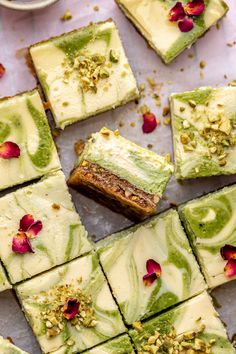 several pieces of green and white cake with flowers on top, surrounded by other desserts