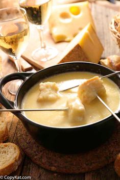 a bowl of soup with cheese and bread on the side, next to wine glasses