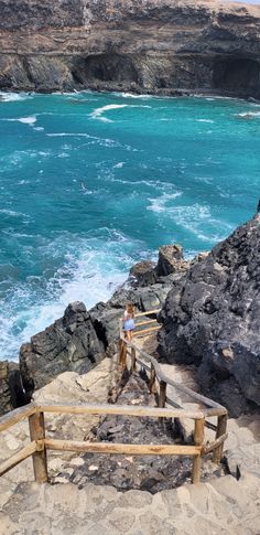 a person standing on top of a rocky cliff next to the ocean with blue water