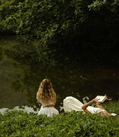 two women are sitting by the water and reading books while looking at something in the distance