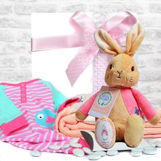 a stuffed rabbit sitting on top of a pile of baby blankets next to a gift box