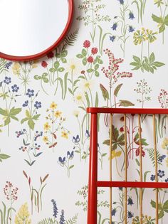 a red chair sitting in front of a wall with flowers on it and a mirror