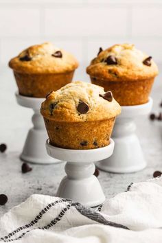 three chocolate chip muffins sitting on top of a white cake stand next to coffee beans