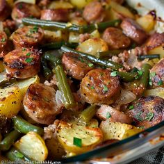 a glass bowl filled with sausage, potatoes and green beans