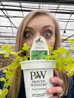 a woman holding up an ice cream cup with plants growing out of it in front of her face