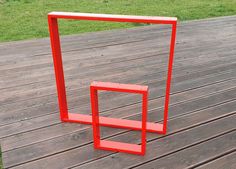 a red sculpture sitting on top of a wooden floor next to a grass covered field