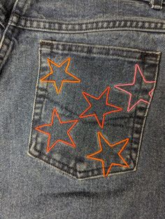 a pair of blue jeans with orange and pink stars on the back pocket, in close up