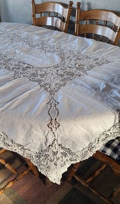 the table cloth is white and has an intricate design on it, along with wooden chairs