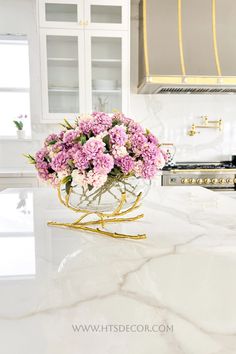 pink flowers are in a glass bowl on the kitchen countertop, next to an oven