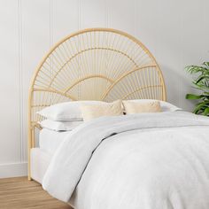 a bed with white linens and a bamboo headboard in a room next to a potted plant