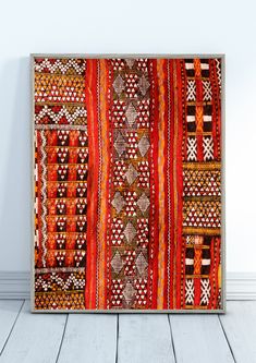 an orange and red rug is hanging on the wall in front of a white wooden floor