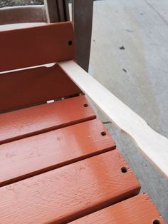 a red wooden bench sitting on top of a sidewalk next to a window sill