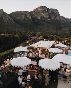 an aerial view of people eating and drinking under white umbrellas in front of mountains