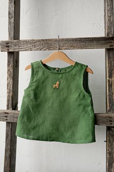 Sleeveless unisex shirt with a coconut button in the back is made of 100% soft medium weight linen. The shirt is suitable for both girls and boys.  Details: - Choose size and embroidery in the drop down menu - Colour: Apple green - Composition: 100% Oeko-Tex certified linen - Coconut button in the back - Medium weight linen - Unisex  - Relaxed silhouette - Linen care: machine wash gentle; tumble dry low, ironing optional - The price is for one shirt, other pictured items are not included Green Cotton Vest Top, Summer Sleeveless Cotton Blouse, Green Linen Tops For The Beach, Green Linen Beach Top, Green Sleeveless Linen Top, Green Sleeveless Cotton Blouse, Embroidery Kids Clothes, Linen Kids Clothes, Boys Linen Shirt