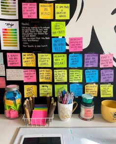 a desk with many sticky notes on the wall next to a cup and pen holder