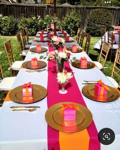 a long table set up with place settings and pink, orange and yellow napkins