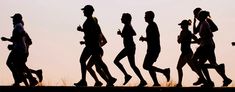 silhouettes of people running in the sun at dusk or dawn, with one person on his cell phone