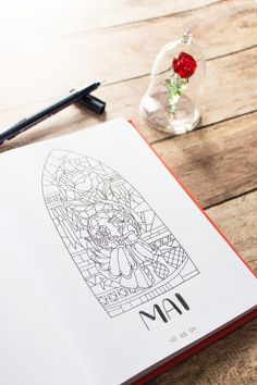 an open book on a wooden table next to a pen and flower