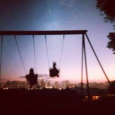 two people are swinging on swings in the evening