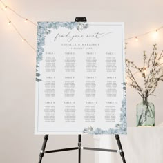 a white and blue wedding seating chart on a easel with lights in the background