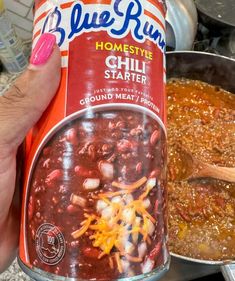 a person holding a can of chili next to a pot full of beans and cheese