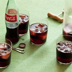 three glasses filled with red liquid next to a bottle of coca cola on a table